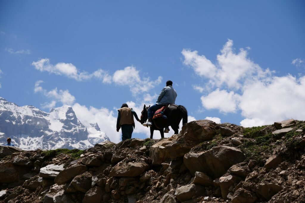 Local guide on horseback on a rocky ridge above Fairy Meadows with snow-capped Nanga Parbat peaks behind, northern Pakistan