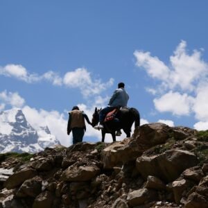 Local guide on horseback on a rocky ridge above Fairy Meadows with snow-capped Nanga Parbat peaks behind, northern Pakistan