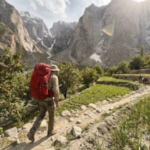 Solo trekker on the narrow rocky trail through Hushe Valley approaching Nangma Valley, terraced fields and towering mountain walls, Skardu Pakistan