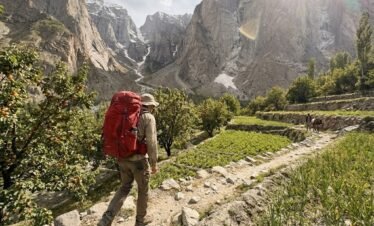Solo trekker on the narrow rocky trail through Hushe Valley approaching Nangma Valley, terraced fields and towering mountain walls, Skardu Pakistan