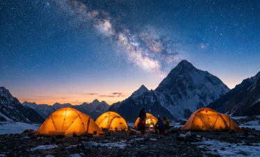 A cinematic night view of a mountain camp where several tents glow with warm light from within, set against the backdrop of the Milky Way and the dark silhouette of K2.