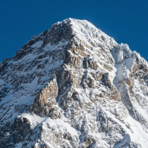 A high-resolution close-up of the K2 summit, showcasing the sharp, icy ridgelines and steep rocky faces of the "Savage Mountain" against a piercing, cloudless blue sky.