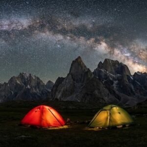 Expedition tents glowing under a dramatic Milky Way sky above the granite peaks of Nangma Valley, high altitude trekking Skardu Pakistan