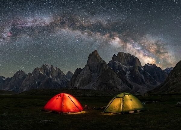 Expedition tents glowing under a dramatic Milky Way sky above the granite peaks of Nangma Valley, high altitude trekking Skardu Pakistan