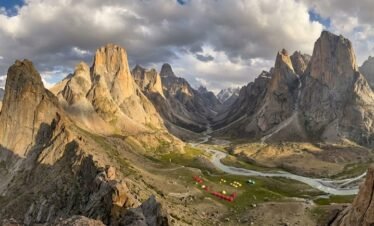 Panoramic ridge view of the entire Nangma Valley below with dramatic granite towers on both sides and expedition tents visible on the valley floor, Skardu Pakistan