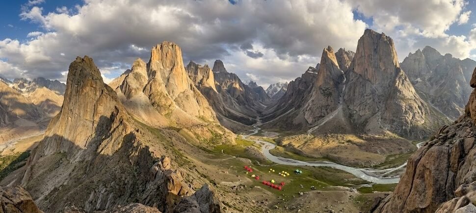 Panoramic ridge view of the entire Nangma Valley below with dramatic granite towers on both sides and expedition tents visible on the valley floor, Skardu Pakistan