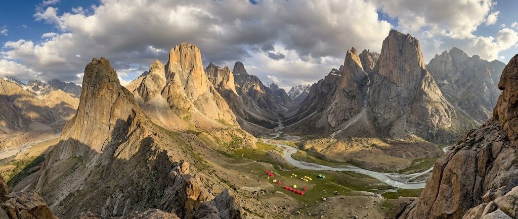 Panoramic ridge view of the entire Nangma Valley below with dramatic granite towers on both sides and expedition tents visible on the valley floor, Skardu Pakistan
