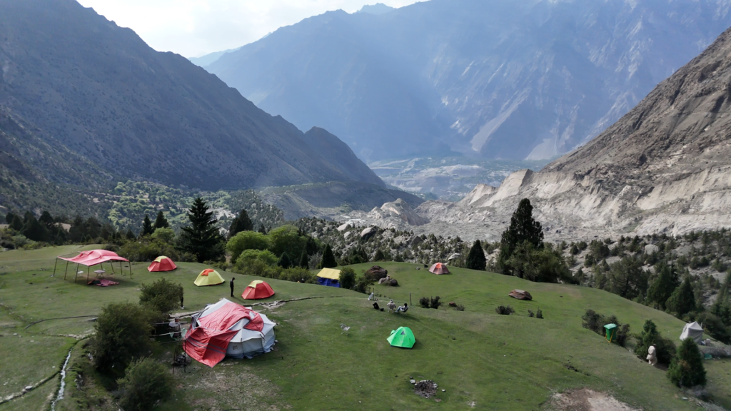Aerial drone view of colourful expedition tents on the hillside above a dramatic Karakoram valley, Rakaposhi Base Camp trek Pakistan