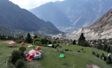 Aerial drone view of colourful expedition tents on the hillside above a dramatic Karakoram valley, Rakaposhi Base Camp trek Pakistan
