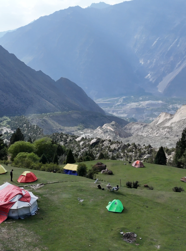 Aerial drone view of colourful expedition tents on the hillside above a dramatic Karakoram valley, Rakaposhi Base Camp trek Pakistan