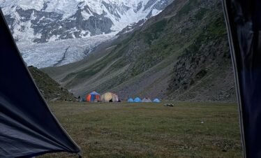 View from inside a tent at Rakaposhi Base Camp looking across the campsite to the towering snow-capped Rakaposhi peak, northern Pakistan