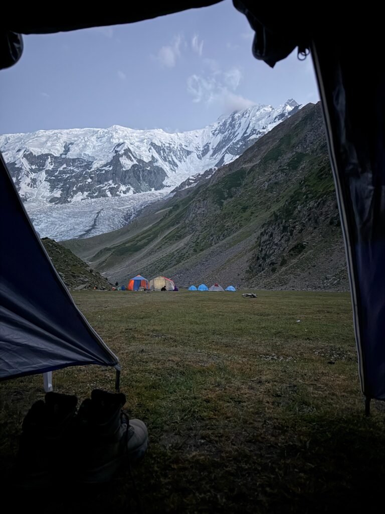 View from inside a tent at Rakaposhi Base Camp looking across the campsite to the towering snow-capped Rakaposhi peak, northern Pakistan
