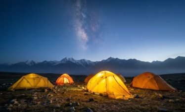 Expedition tents pitched on the Shimshal Pamir plateau at dusk with the Milky Way above snow-capped peaks, high altitude trekking Pakistan