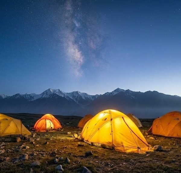 Expedition tents pitched on the Shimshal Pamir plateau at dusk with the Milky Way above snow-capped peaks, high altitude trekking Pakistan