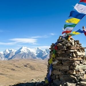 Trekker standing at the summit cairn of Shimshal Pass at 4,735m with prayer flags and vast Pamir plateau stretching behind, northern Pakistan
