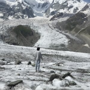 Trekker standing on the Rakaposhi glacier with the massive 7,788m Rakaposhi summit towering behind, northern Pakistan