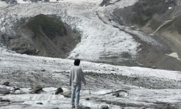 Trekker standing on the Rakaposhi glacier with the massive 7,788m Rakaposhi summit towering behind, northern Pakistan