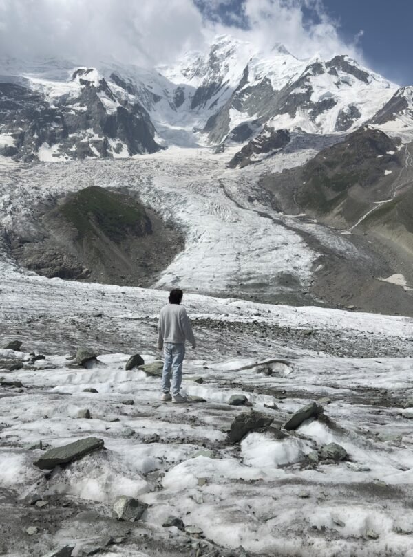 Trekker standing on the Rakaposhi glacier with the massive 7,788m Rakaposhi summit towering behind, northern Pakistan