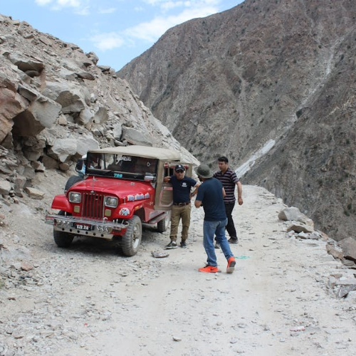 A red jeep navigates the high-altitude Fairy Meadows jeep track in Gilgit-Baltistan, Pakistan. This iconic route runs from Raikot Bridge to Tato Village, climbing through dramatic mountain passes with sheer rock walls and river valleys. The Fairy Meadows jeep track is the gateway to the Nanga Parbat Base Camp trek and offers one of northern Pakistan's most thrilling alpine driving experiences.
